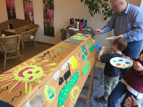 Kind bemalt die Sargseite mit Sonne, Vögeln und bunten Motiven