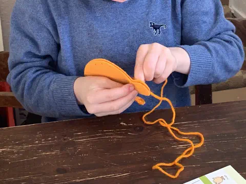 Kinderhände beim Zusammennähen eines orangefarbenen Filz-Organs