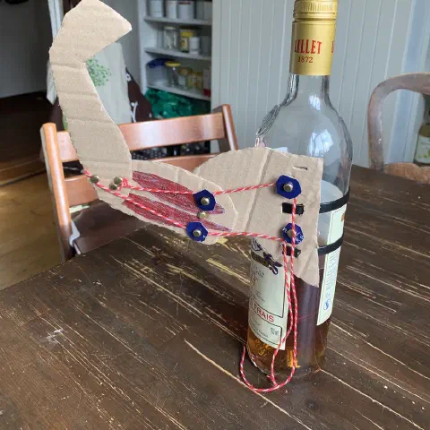 Greifarm aus Pappe und Musterklammern an einer Flasche