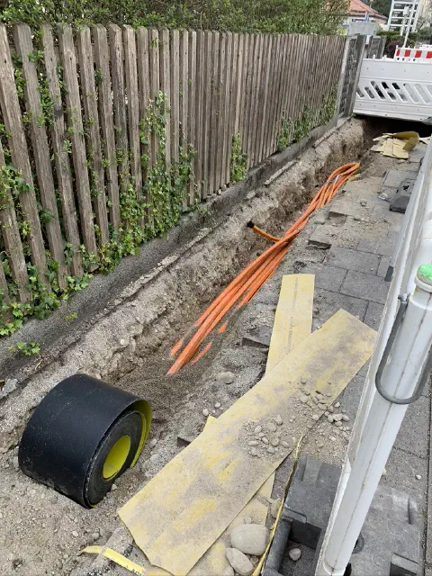 Verlegung orangefarbener Glasfaserkabel im Graben entlang eines Holzzauns