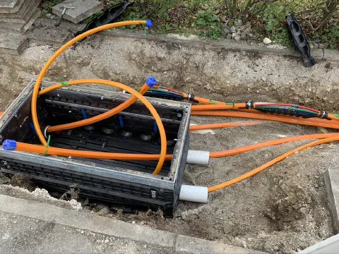 Glasfaser-Muffe mit mehreren angeschlossenen orangefarbenen Kabeln in der Baugrube