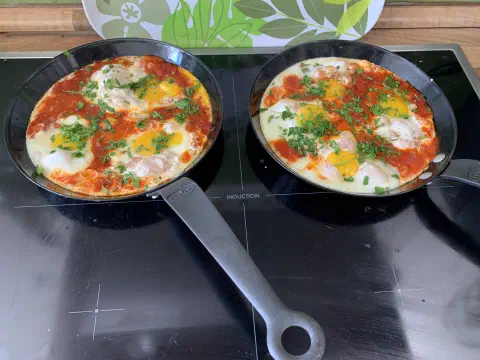 Zwei Pfannen Shakshuka mit pochierten Eiern in Tomatensauce auf dem Herd