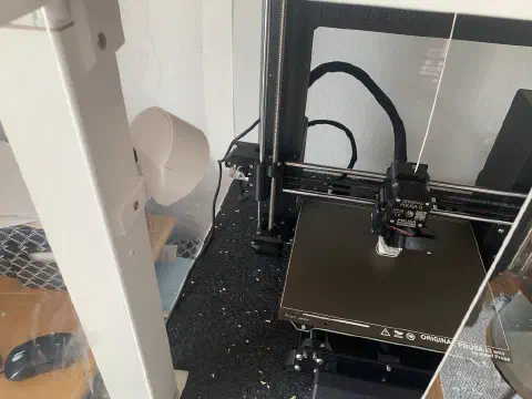 Prusa 3D-Drucker im Ikea-Lack-Gehäuse mit montierter Kamerahalterung in der Ecke
