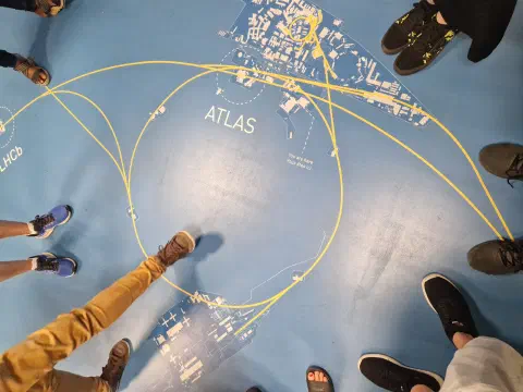 Bodenkarte des LHC-Rings mit ATLAS- und LHCb-Markierungen, umstanden von Besuchern